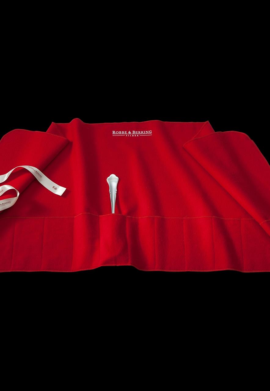 Die Abbildung zeigt eine rote Bestecktasche mit mehreren Fächern. In einem der Fächer steckt ein silbernes Besteckteil.
