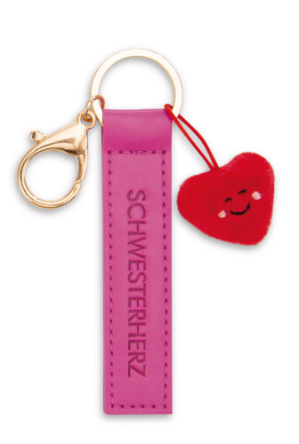 Der Schlüsselanhänger besteht aus einem pinken Band mit der Aufschrift „SCHWESTERHERZ“. Daran hängt ein kleines, rotes Plüschherz mit einem lächelnden Gesicht.