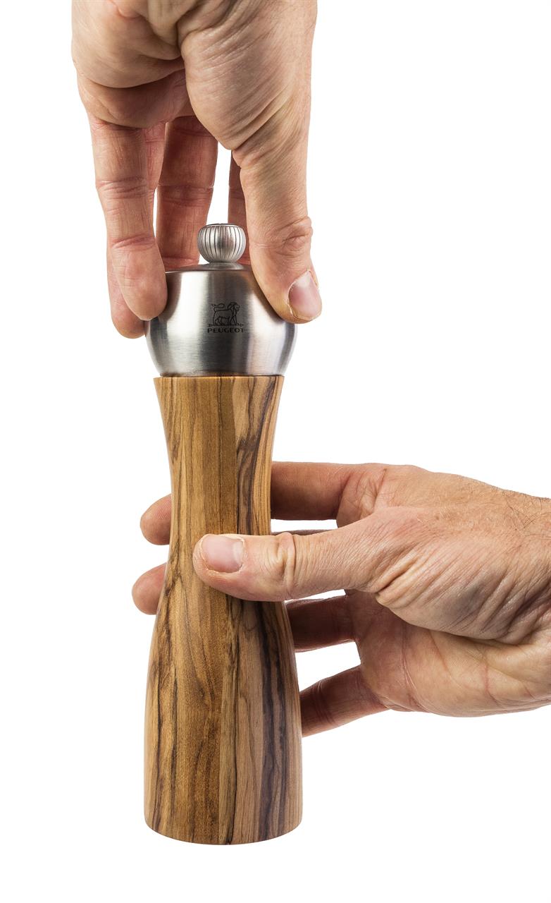 Auf dem Bild ist eine Pfeffermühle aus Olivenholz mit einer Edelstahlkappe zu sehen. Sie wird von zwei Händen gehalten und benutzt.