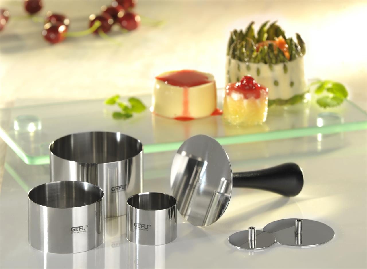 Das Bild zeigt die Profispeisenringe Formidable, 10-teilig, aus Edelstahl von GEFU. Im Hintergrund sind kunstvoll angerichtete Speisen zu sehen, die mit den Ringen in Form gebracht wurden.