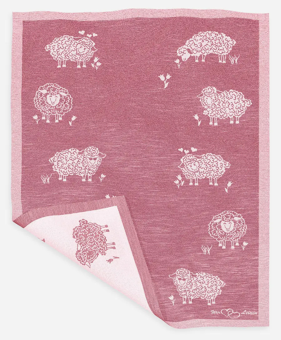 Das Bild zeigt ein rotes Halbleinen-Geschirrtuch mit dem Namen "Molly" in der Größe 45x73 cm. Auf dem Tuch sind mehrere weiße Schafe und kleine Blumen abgebildet.