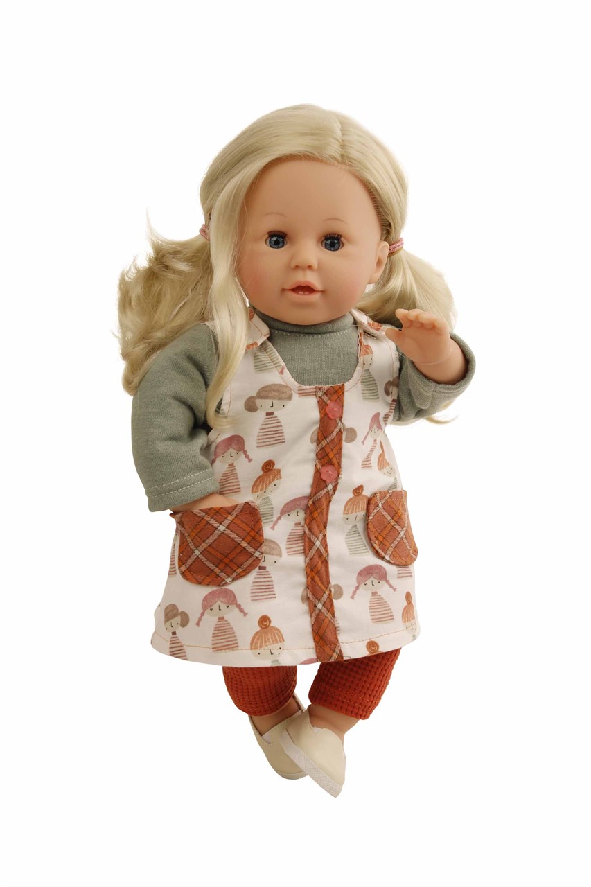 Die Puppe hat blonde Haare und blaue Schlafaugen. Sie trägt eine Latzhose mit Puppenmotiv und roten Hosen.