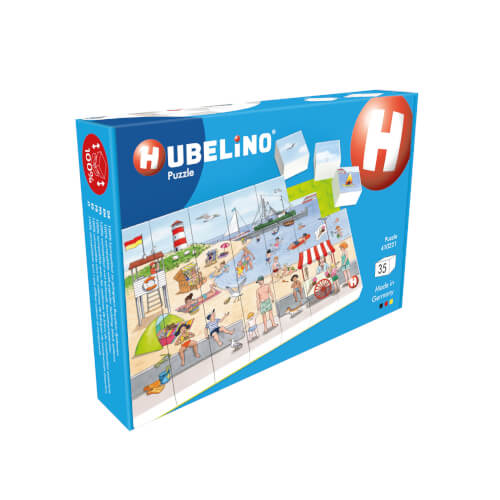 Auf dem Bild ist eine Hubelino-Puzzle-Verpackung zu sehen. Das Motiv des Puzzles zeigt eine bunte Strandszene mit vielen spielenden Menschen.