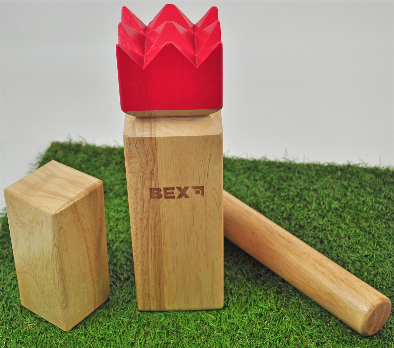 Das Bild zeigt das Produkt "Kubb Pro Rubberwood Red King" auf einem Stück Kunstrasen. In der Mitte steht der große Holzkönig mit einer roten Krone, daneben liegen weitere Kubb-Spielsteine.