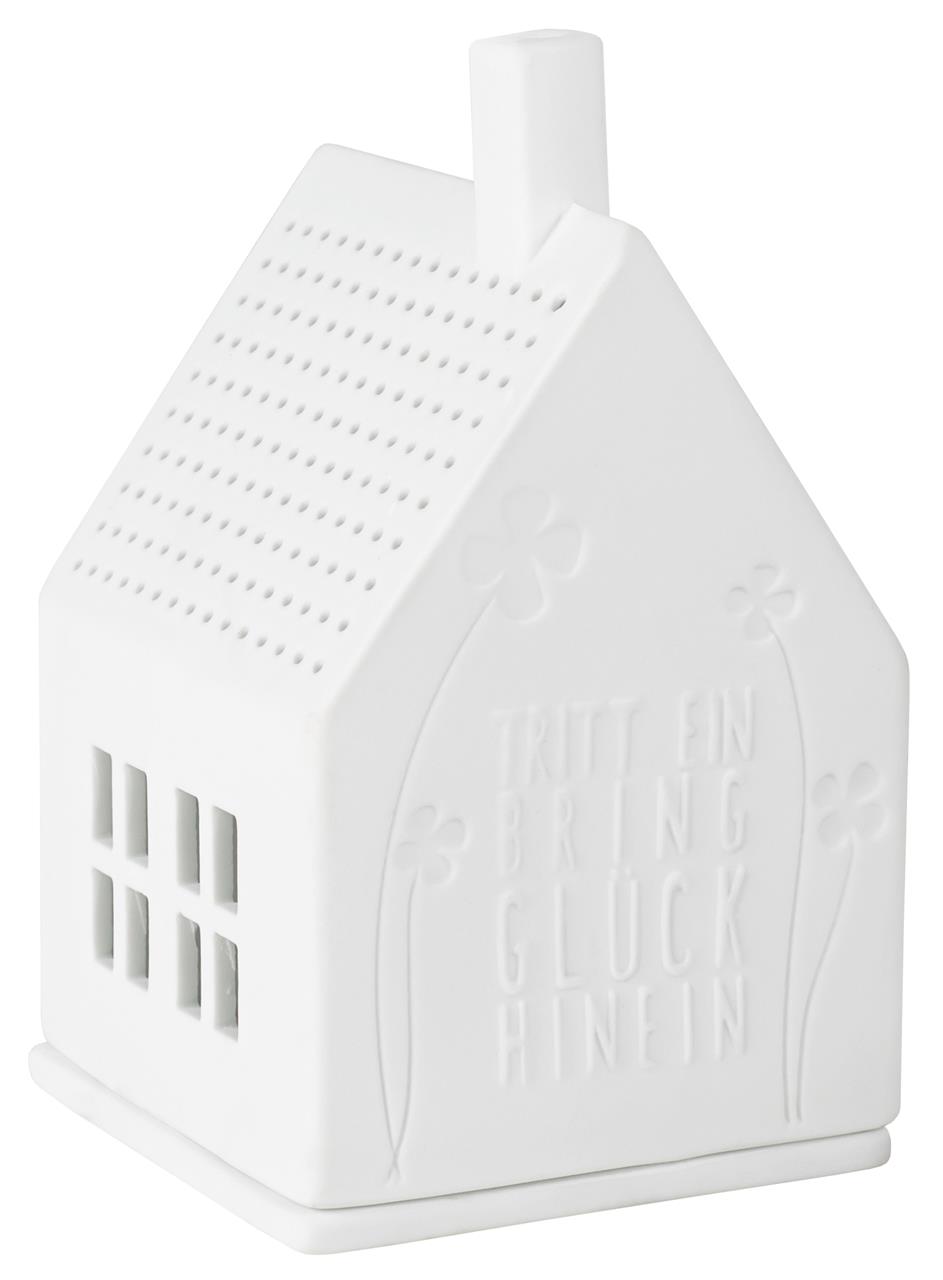 Das Bild zeigt ein kleines, weißes Lichthaus aus Porzellan in Form eines Hauses. Auf der Vorderseite steht der Schriftzug „Tritt ein bring Glück hinein“ und es sind Blumendetails eingraviert.