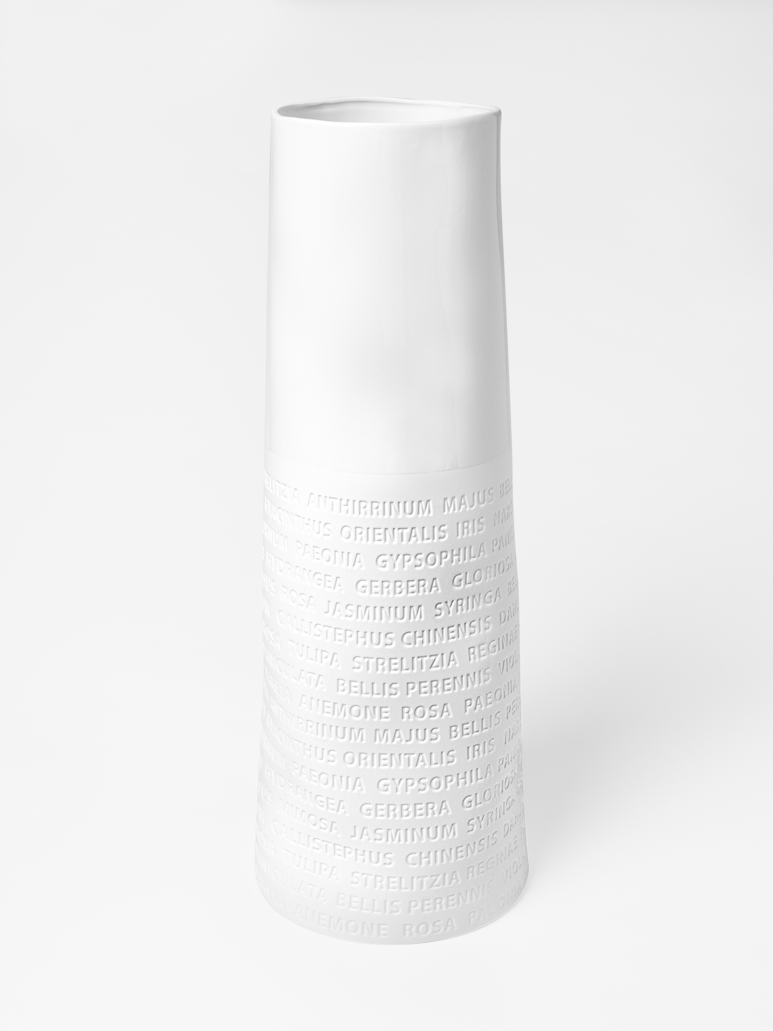 Die Abbildung zeigt eine hohe, weiße Bodenvase mit zylindrischer Form. Im unteren Bereich der Vase sind Buchstaben und Wörter erhaben eingearbeitet.