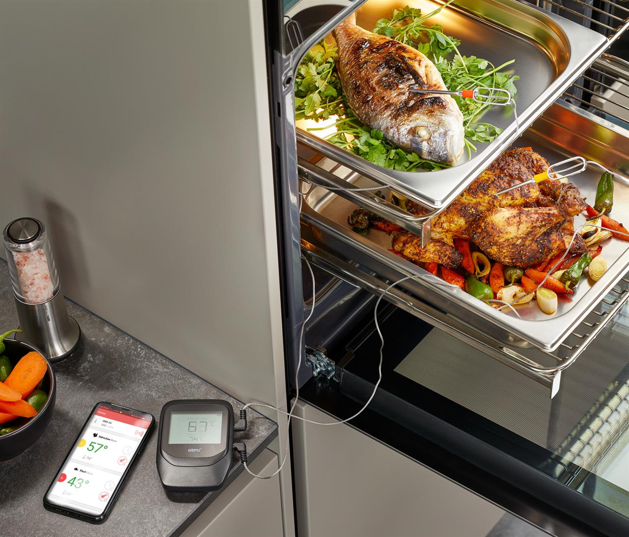 Das Bild zeigt das Grill- und Bratenthermometer Control+ 6 Kanal mit 2 Sonden im Einsatz im Ofen. Ein Handy und das Thermometer zeigen die aktuellen Temperaturen der Speisen an.