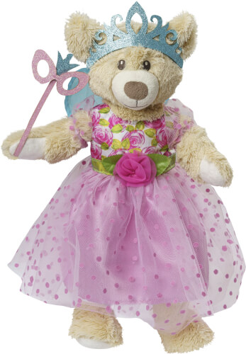 Ein Plüschteddy trägt ein rosa Kleid mit Punkten und eine blaue Krone. In der Pfote hält er einen Zauberstab mit einer rosa Maske.