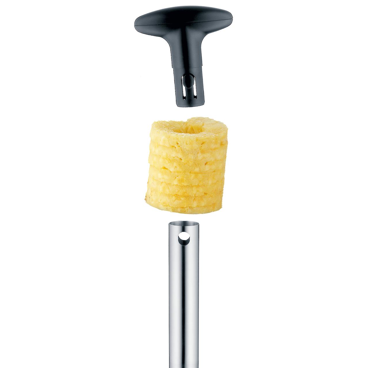 Das Bild zeigt einen Ananasschneider mit einem spiralförmig geschnittenen Stück Ananas. Der Griff des Schneiders ist vom Metallstab abgenommen und schwebt darüber.
