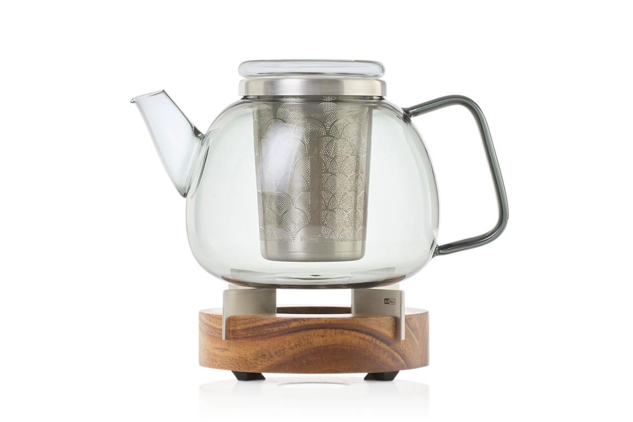 Die Abbildung zeigt eine Teekanne aus Glas mit einem Edelstahlsieb und einem passenden Stövchen aus Holz. Das Set wirkt modern und elegant, ideal zum stilvollen Teegenuss.