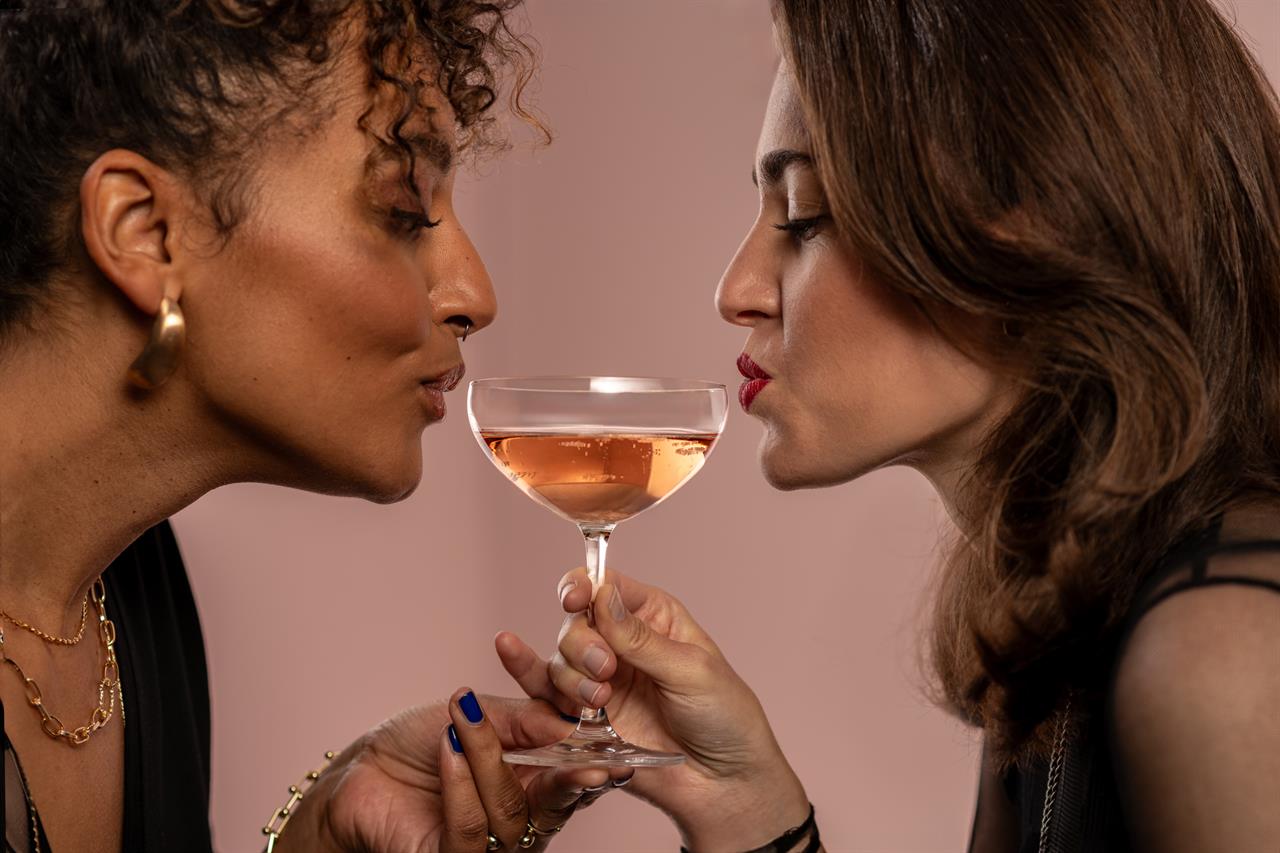 Zwei Frauen halten gemeinsam ein Sektglas, das mit einem roséfarbenen Getränk gefüllt ist. Sie führen ihre Lippen nah an das Glas der '4er Sektschale Bar Special 8'.