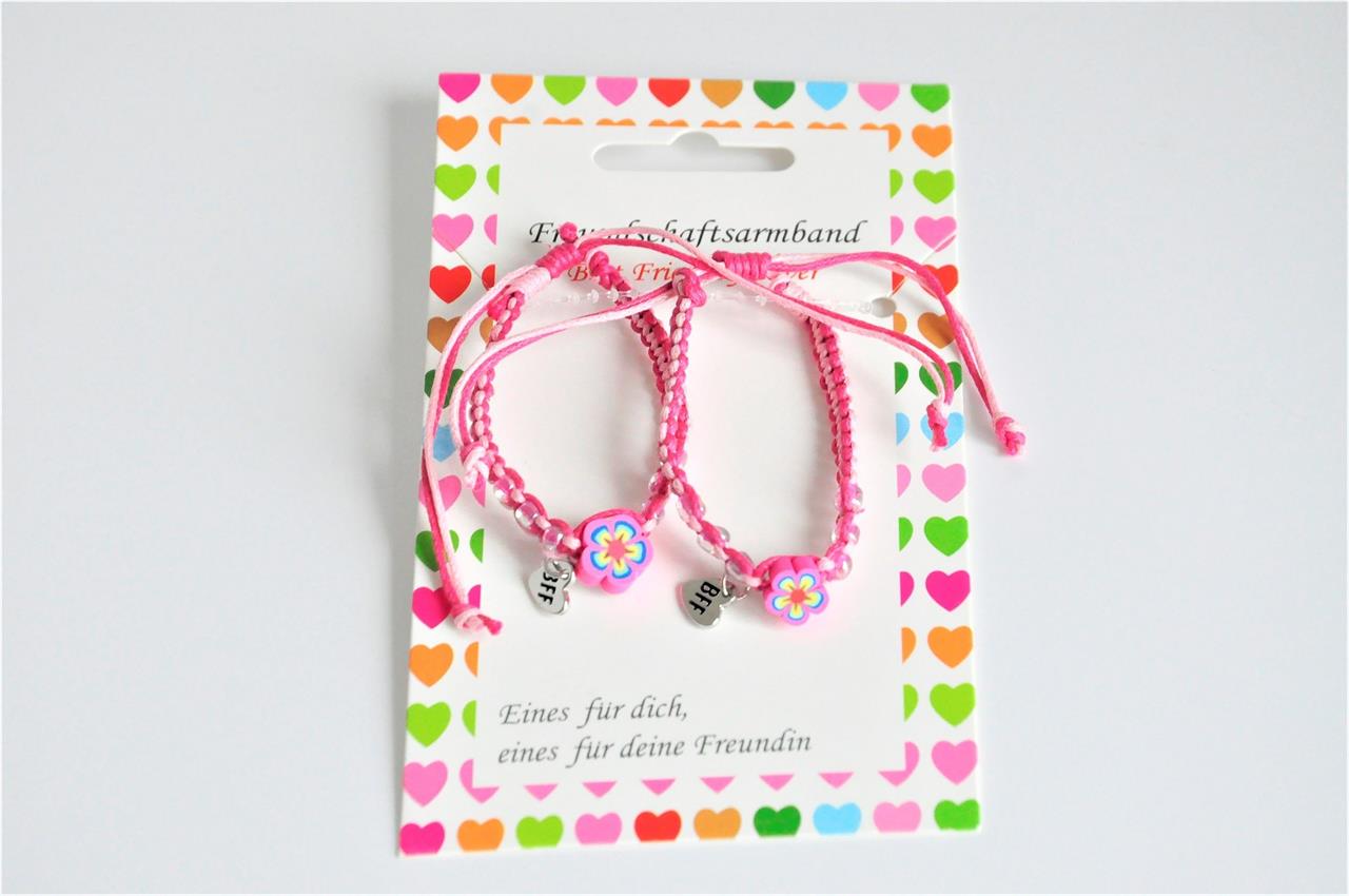 Das Bild zeigt zwei pinke Freundschaftsarmbänder mit kleinen Blumen aus Fimo. Sie sind auf einer Karte mit bunten Herzen befestigt und tragen jeweils einen "BFF"-Anhänger.
