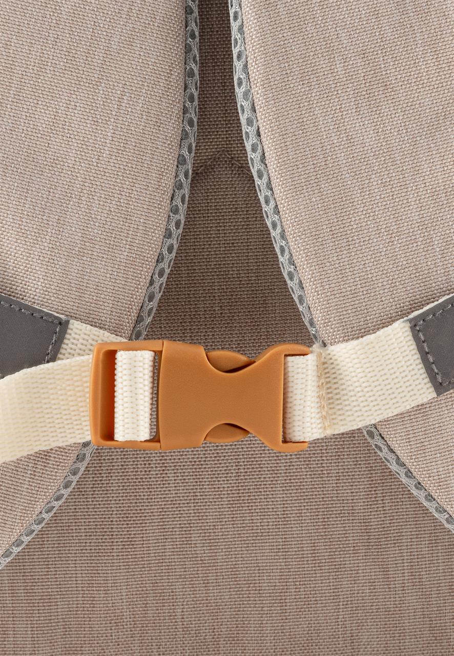 Das Bild zeigt eine Nahaufnahme eines beige-farbenen Kinderrucksacks mit einem hellen Brustgurt und einem braunen Klickverschluss. Die Nähte und das Material des Rucksacks sind gut zu erkennen.