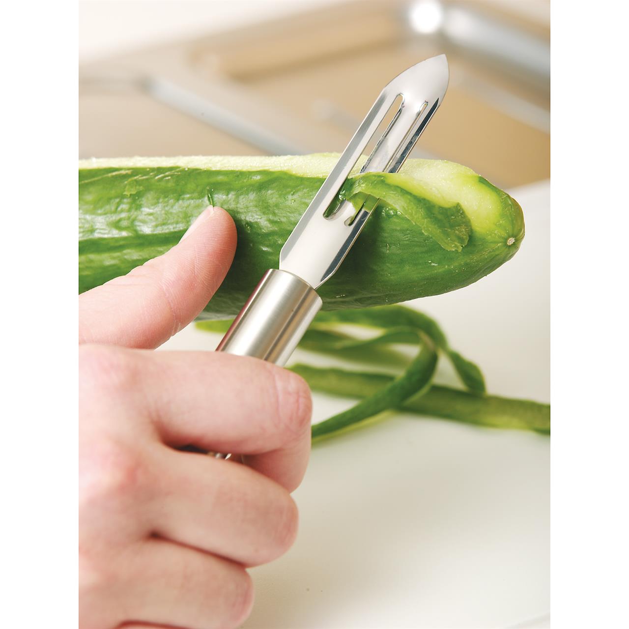 Eine Hand schält eine Gurke mit dem Gemüseschäler Profi Plus. Der Schäler entfernt die Schale in dünnen Streifen.