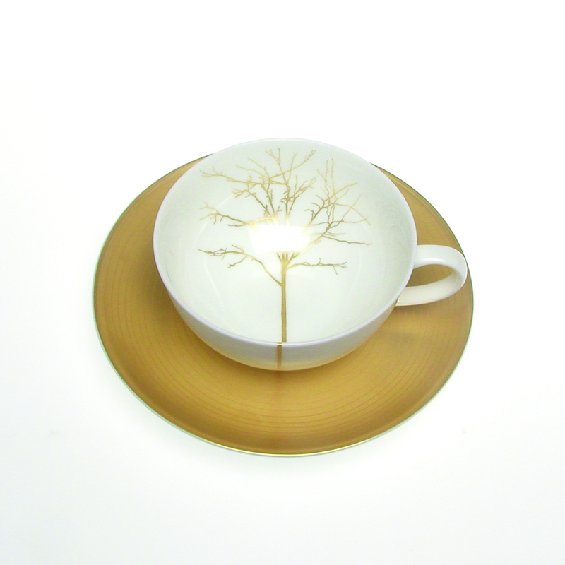 Auf dem Bild ist eine elegante Teetasse aus Fine Bone China mit einem goldenen Baumdesign zu sehen. Die Tasse steht auf einer passenden goldfarbenen Untertasse.