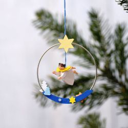 Das Bild zeigt eine Weihnachtsdekoration namens "Engel im Ring". Ein kleiner Engel hängt in einem Ring, der mit Sternen und einer kleinen Baumfigur verziert ist.