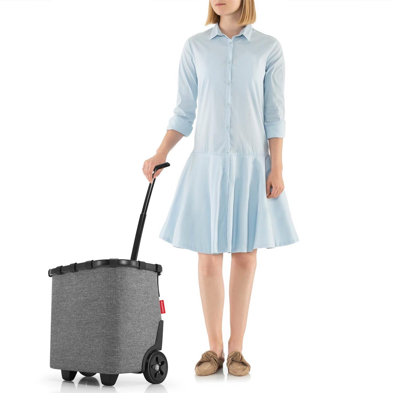 Eine Frau steht neben einem Carrycruiser Frame Twist Silver und hält den Griff fest. Der Einkaufsroller hat ein elegantes, silber-graues Design und zwei große Räder.