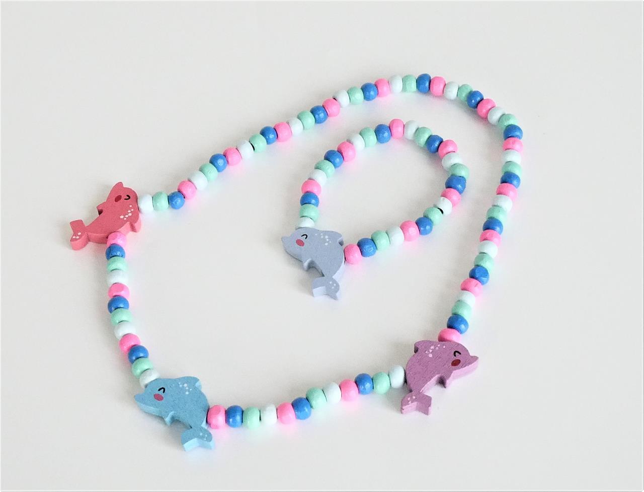 Das Bild zeigt ein Set aus einer Kette und einem Armband aus bunten Holzperlen. Beide Schmuckstücke sind mit kleinen Delfin-Anhängern verziert.