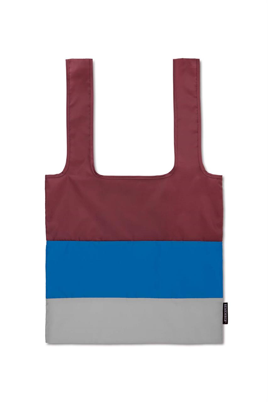 Die Tragetasche faltbar Ava ist in drei Farben gestaltet: Bordeauxrot, Blau und Grau. Sie hat ein einfaches, rechteckiges Design mit zwei Henkeln.