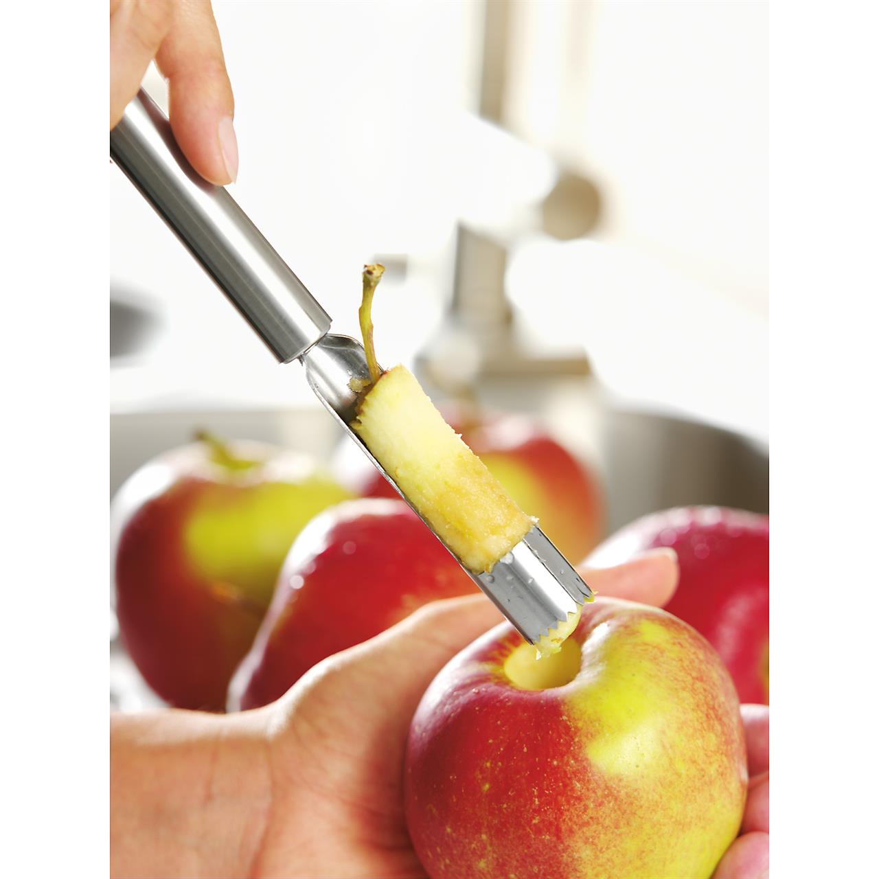 Das Bild zeigt einen Apfelausstecher, der gerade das Kerngehäuse aus einem Apfel entfernt. Im Hintergrund sind weitere Äpfel zu sehen.