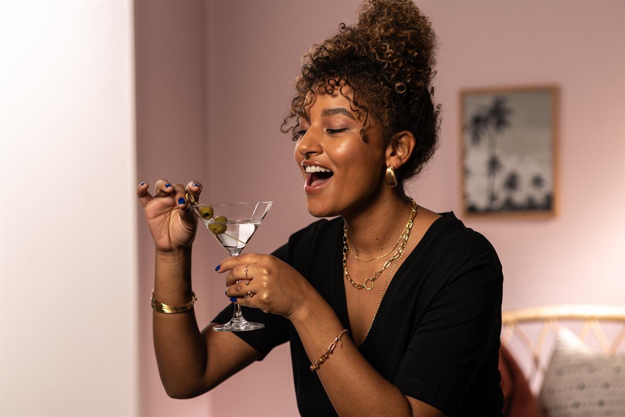 Eine Frau hält ein Martini-Glas mit Oliven und lächelt dabei fröhlich. Das Bild zeigt das Produkt "4er Martini Bar Special 86".