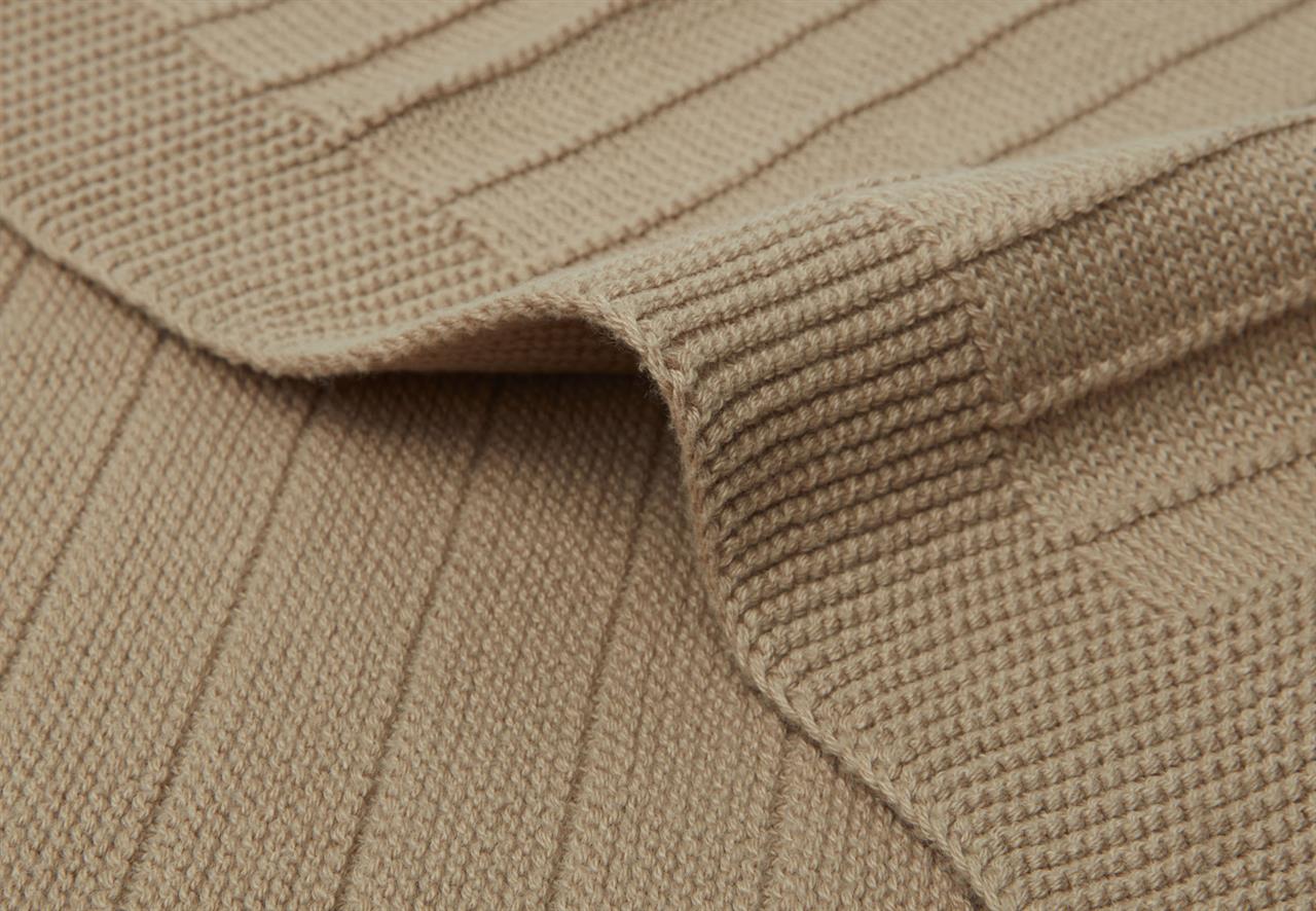 Die Abbildung zeigt eine beige Strickdecke mit feinem Rippenmuster. Die Decke wirkt weich und kuschelig, ideal für Babys oder Kleinkinder.
