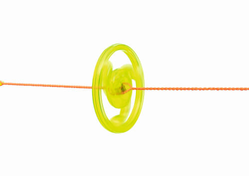 Auf dem Bild ist ein gelbes Jo-Jo zu sehen, das an einer orangefarbenen Schnur hängt. Der Hintergrund ist komplett weiß.