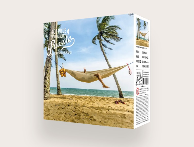 Das Bild zeigt das Produkt 'Puzzle Beach Hammock 1000 Teile'. Es handelt sich um ein Puzzle mit Motiv einer Hängematte am Strand.