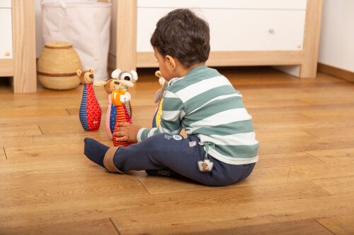 Ein kleines Kind sitzt auf dem Boden und spielt mit buntem Spielzeug. Es trägt ein gestreiftes Oberteil und dunkle Hose.