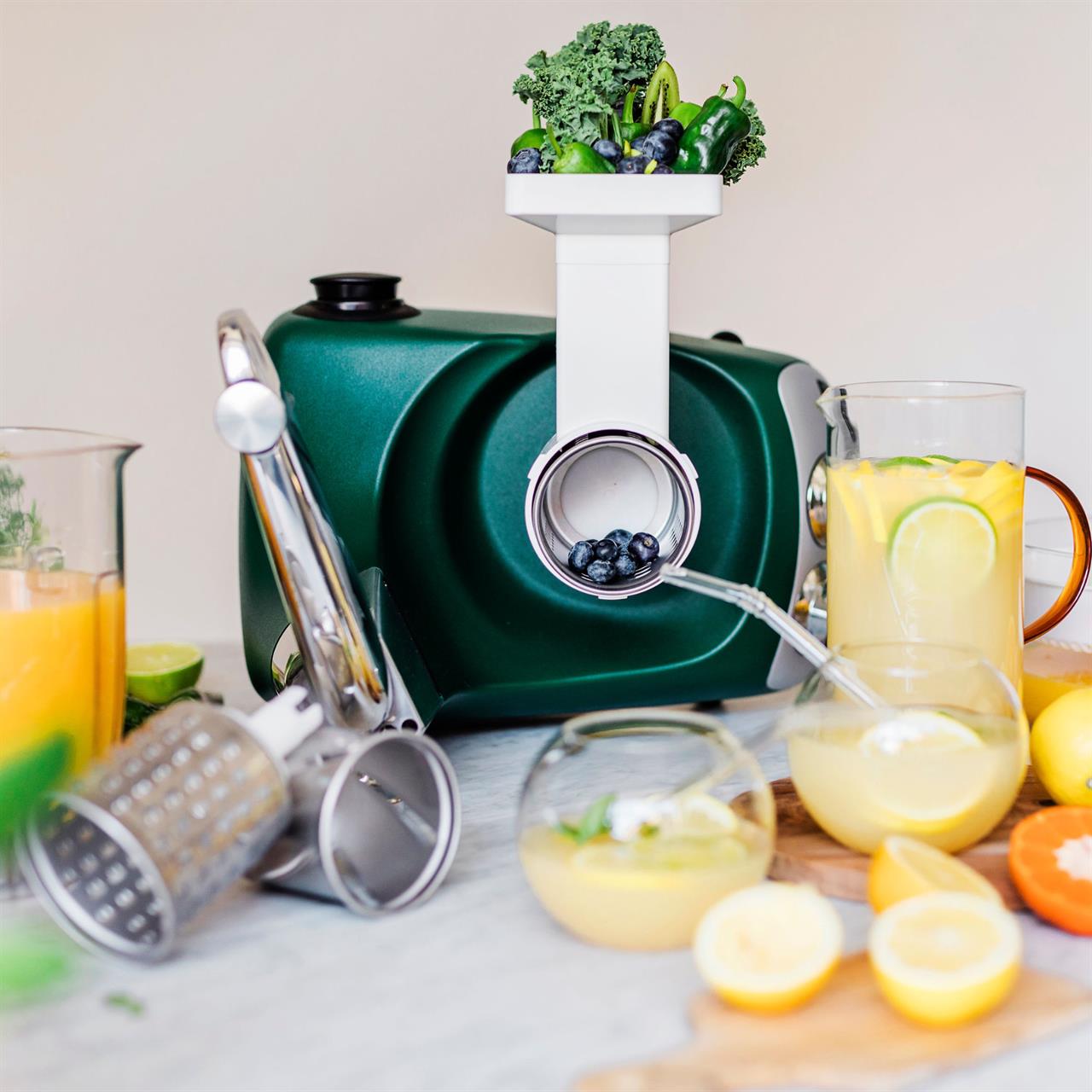 Das Bild zeigt das Produkt „Go Green Package“, eine moderne Saftpresse mit grünem Gehäuse. Frisches Obst und Gemüse sowie Gläser mit frisch gepresstem Saft sind um die Maschine angeordnet.