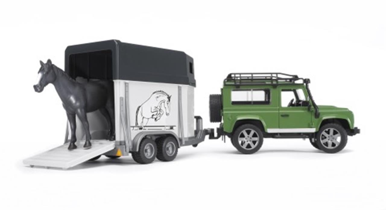 Auf dem Bild ist ein grüner Land Rover Defender mit einem Anhänger zu sehen. Aus dem Anhänger kommt ein schwarzes Pferd heraus.