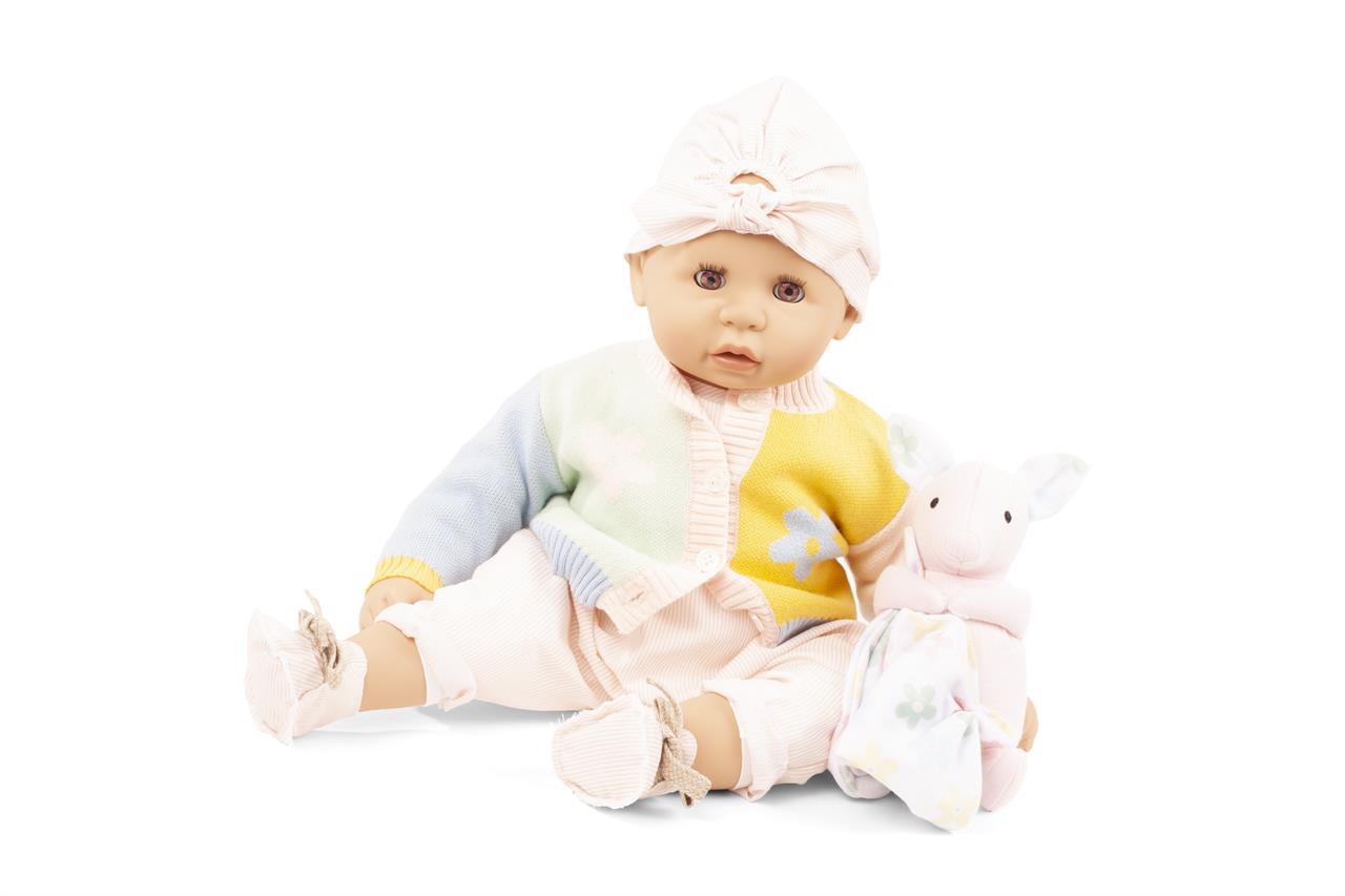 Die Puppe "Cookie, Farbspiel" trägt bunte Kleidung und eine Mütze. Neben ihr sitzt ein kleines, rosa Stofftier mit einem Tuch.