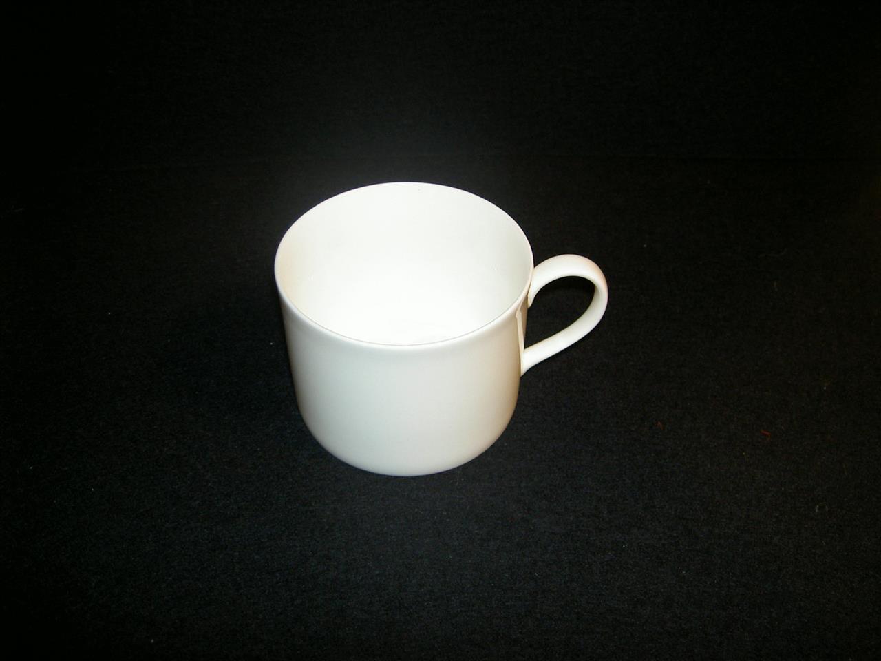 Die Abbildung zeigt eine zylindrische, weiße Espresso-Obertasse aus Fine Bone China mit einem Fassungsvermögen von 0,10 l. Die Tasse hat einen schlichten Henkel und steht vor schwarzem Hintergrund.