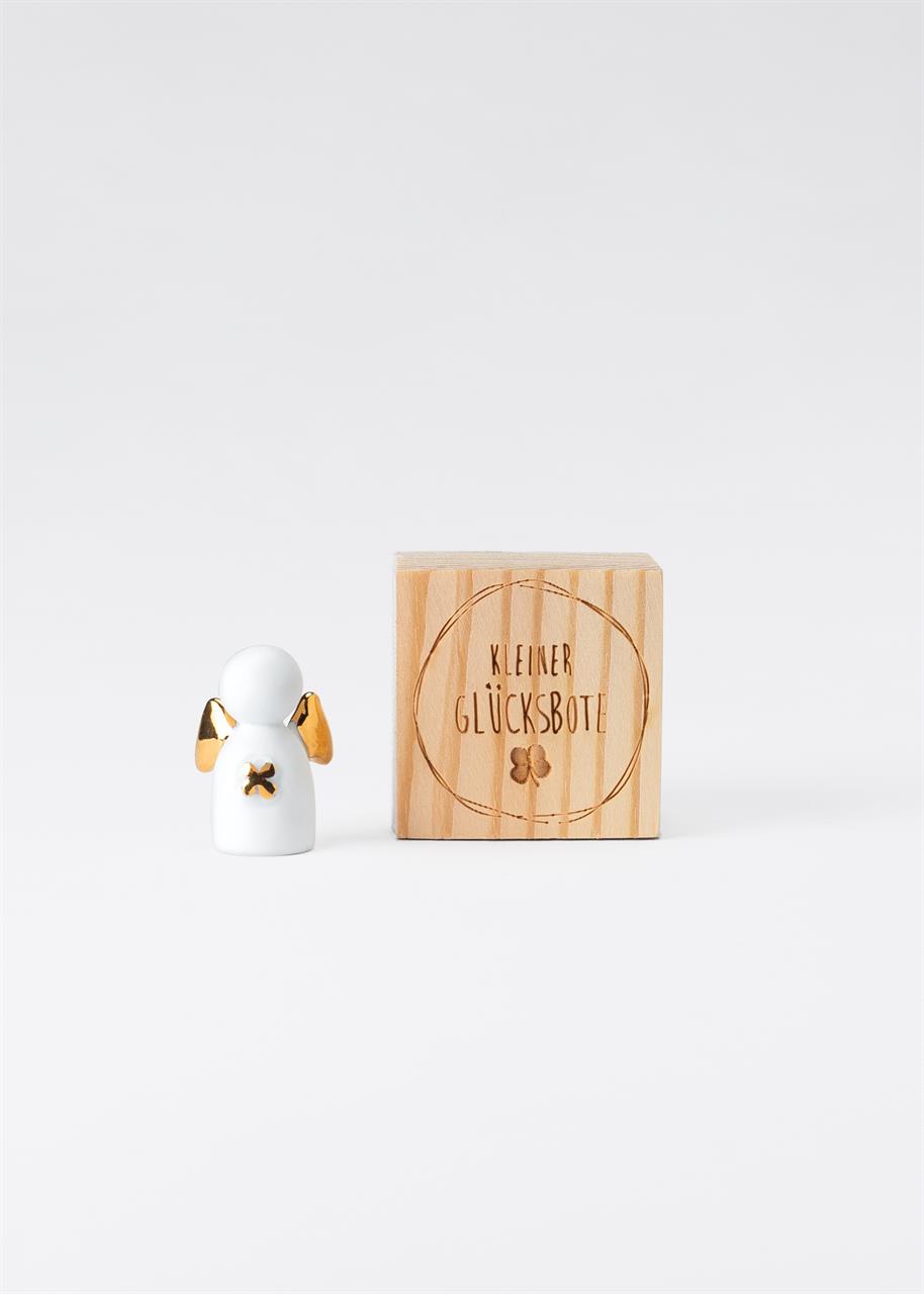 Auf dem Bild ist eine kleine Figur mit goldenen Flügeln zu sehen. Daneben steht eine Holzkiste mit der Aufschrift "Kleiner Glücksbote".