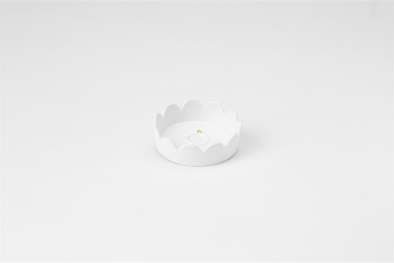 Die Abbildung zeigt eine kleine, weiße Schmuckschale mit gewelltem Rand. In der Mitte der Schale befindet sich ein kleiner goldener Akzent.