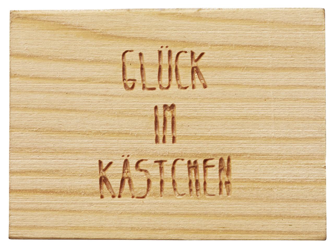 Das Bild zeigt eine kleine Holzkiste mit der Gravur „Glück im Kästchen“. Es handelt sich um das Produkt „Glücksschwein to go“.