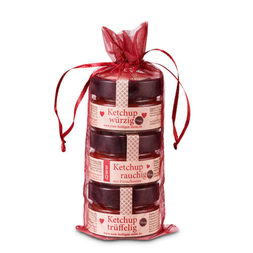 Das Bild zeigt drei Gläser Ketchup in einer roten Geschenkverpackung. Die Sorten sind würzig, rauchig und trüffelig.