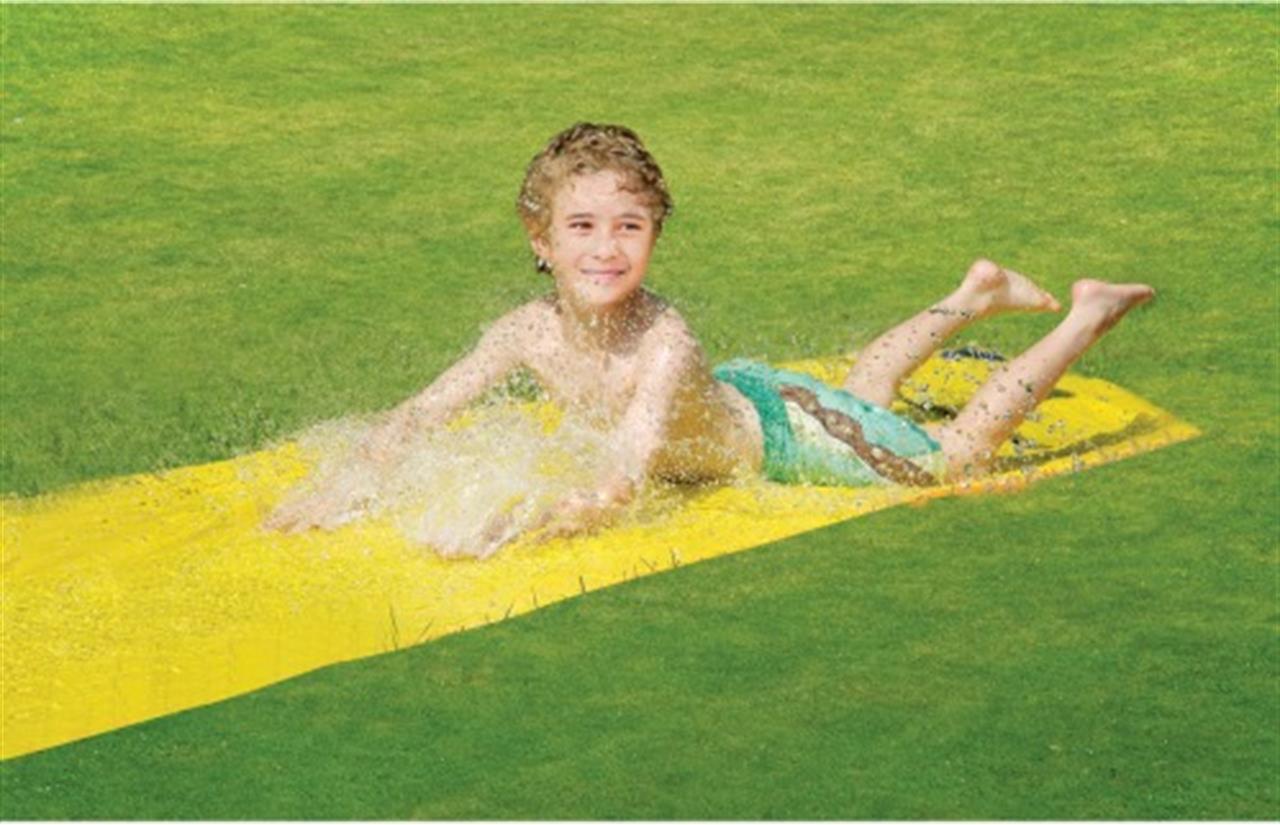 Ein Junge rutscht lachend auf einer gelben Wasserrutsche über den Rasen. Die Wasserrutsche ist etwa 600 x 80 cm groß.