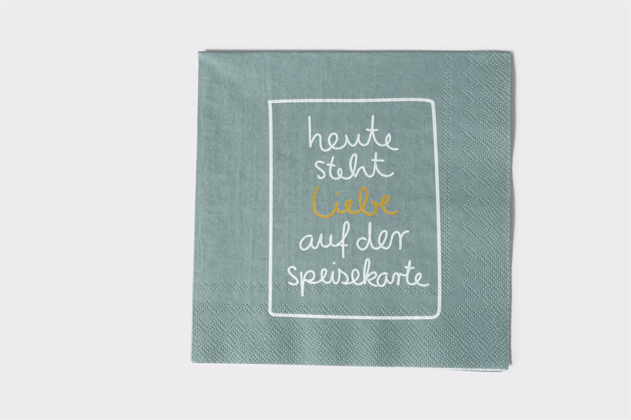 Die Serviette ist grau-grün und hat eine Größe von 33x33 cm. Auf der Serviette steht in weißer und gelber Schrift: "heute steht liebe auf der speisekarte".