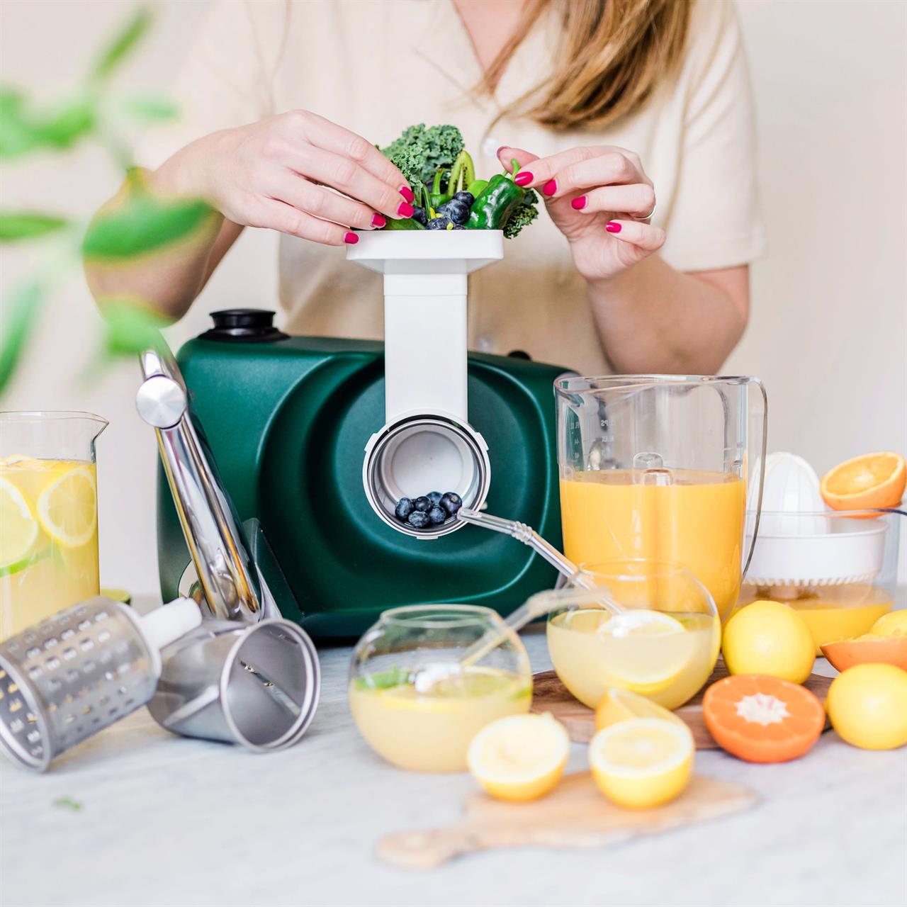 Eine Person bereitet frisches Gemüse und Obst in einem Entsafter aus dem "Go Green Package" zu. Auf dem Tisch stehen verschiedene Säfte, Zitrusfrüchte und Küchenzubehör.
