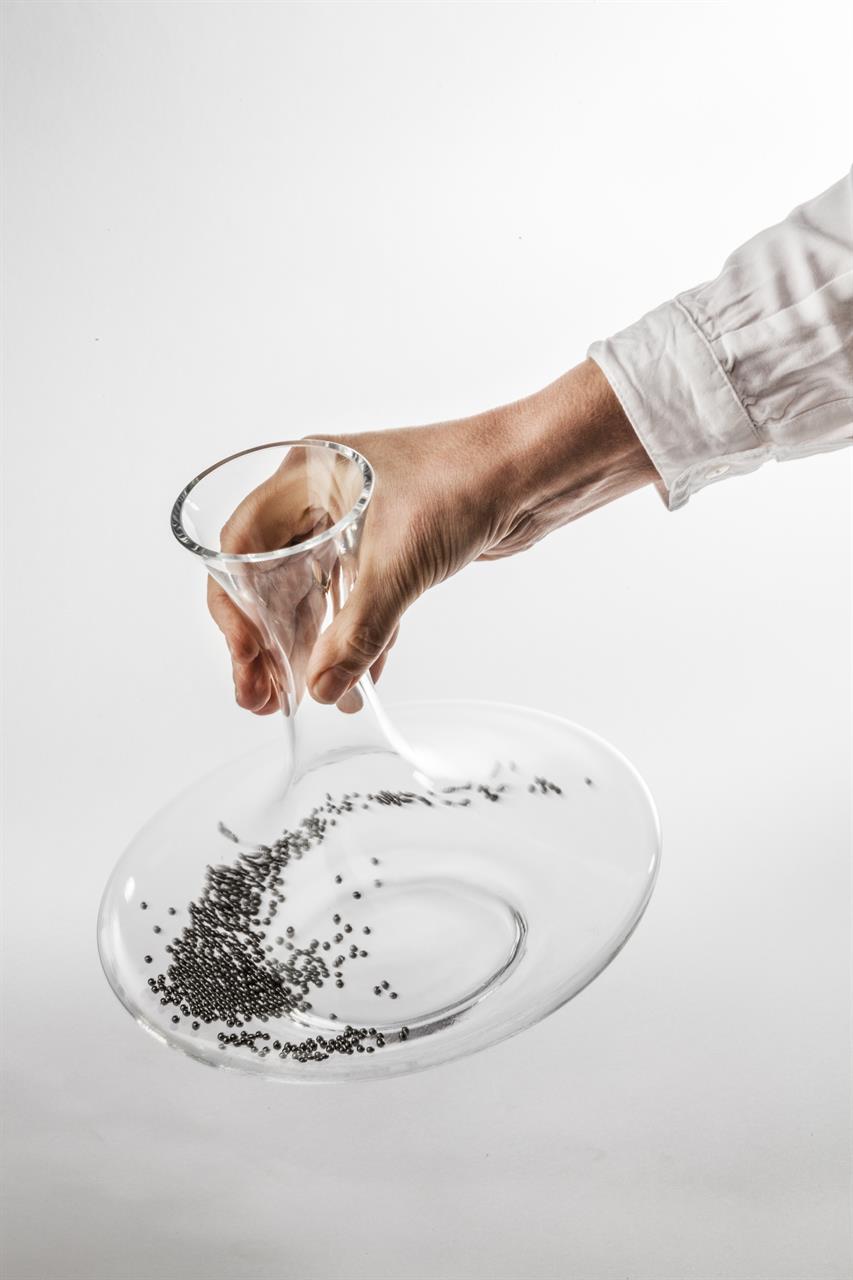 Eine Hand hält eine bauchige Glaskaraffe, in der viele kleine Reinigungskugeln liegen. Die Kugeln werden zur Reinigung von Dekantern verwendet.
