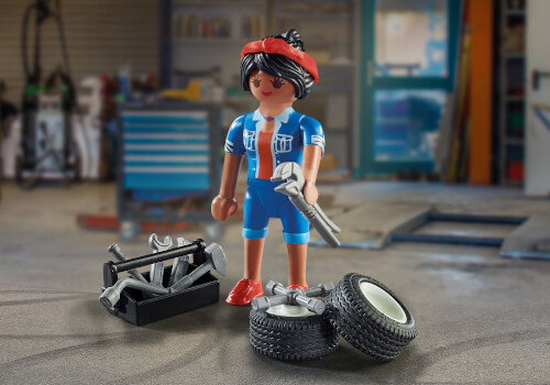 Eine Playmobil-Figur steht in einer Werkstatt und hält einen Schraubenschlüssel in der Hand. Neben ihr liegen Autoreifen und ein Werkzeugkasten mit verschiedenen Werkzeugen.