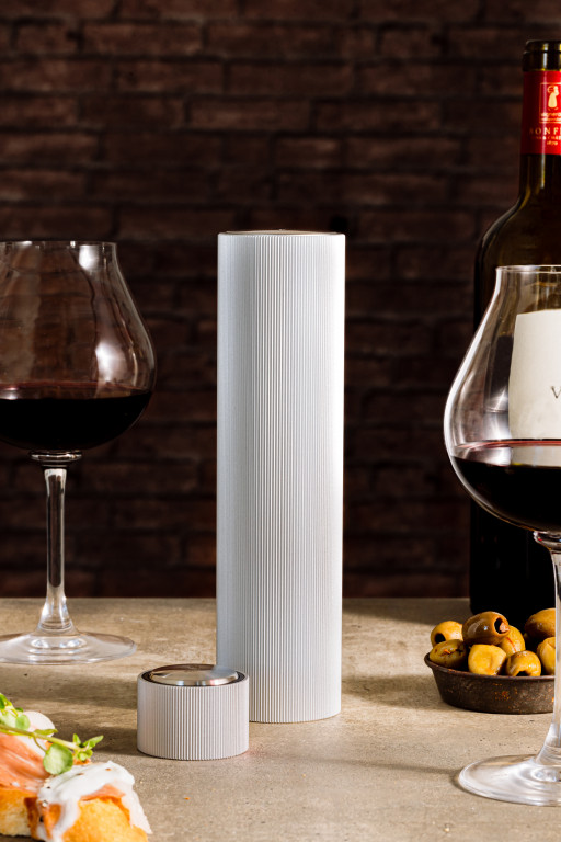 Das Bild zeigt den elektrischen Korkenzieher „Korkenzieher Aluminium Line Reverse“. Er steht auf einem Tisch zwischen zwei Gläsern Rotwein, einer Weinflasche, Oliven und einem Stück Brot.