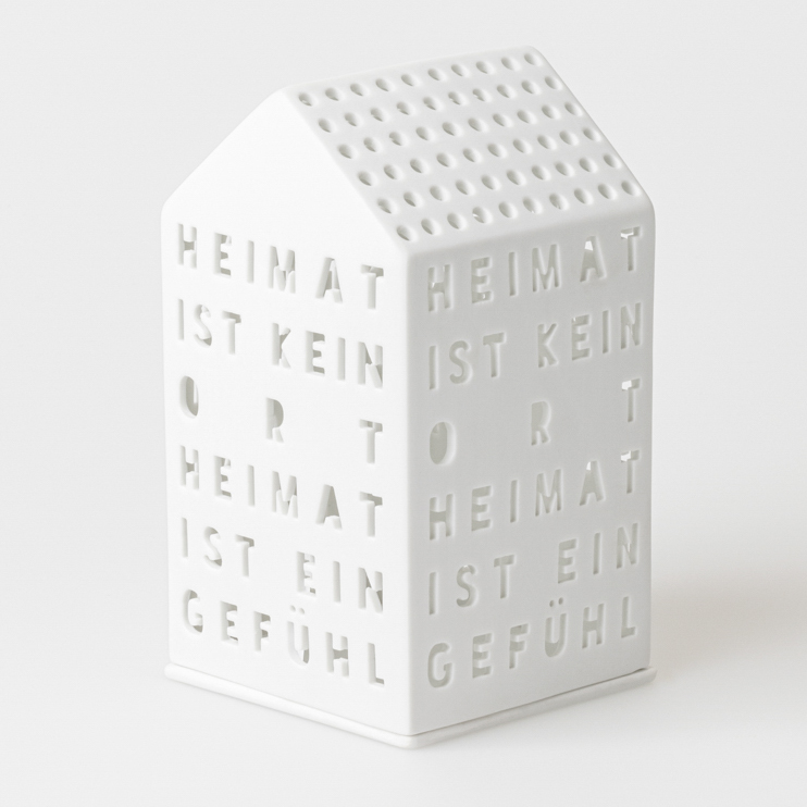 Das Bild zeigt ein weißes, hausförmiges Objekt mit ausgestanzten Buchstaben. Darauf steht: "HEIMAT IST KEIN ORT, HEIMAT IST EIN GEFÜHL."