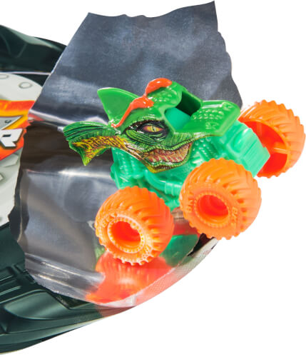 Das Bild zeigt ein kleines Spielzeugauto, das wie ein grüner Dinosaurier aussieht. Es hat vier leuchtend orangefarbene Räder und fährt über eine silberne Bahn.