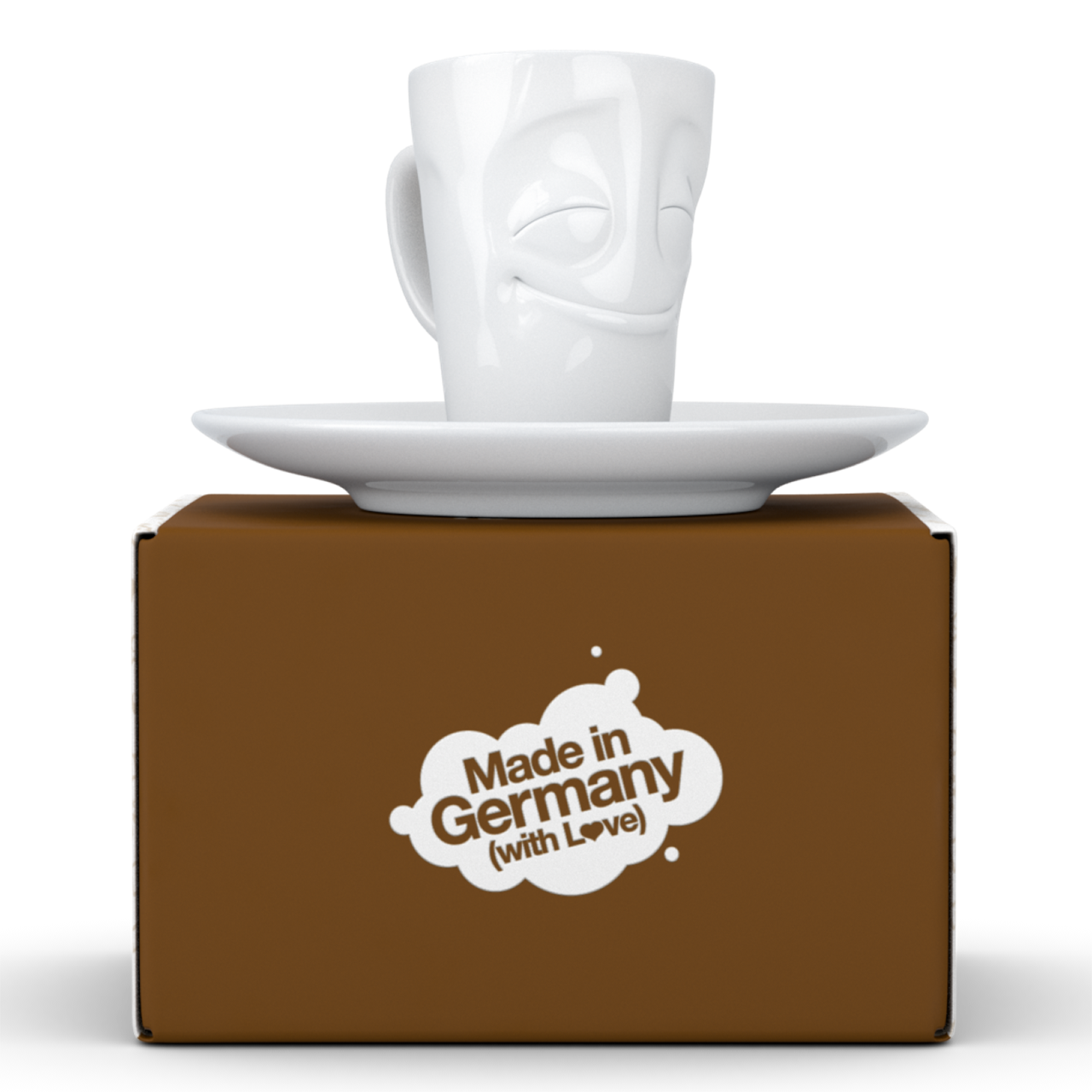 Auf dem Bild ist eine weiße Espresso-Tasse mit dem Namen "Vergnügt" auf einer Untertasse zu sehen. Die Tasse steht auf einer braunen Verpackung mit der Aufschrift "Made in Germany (with Love)".