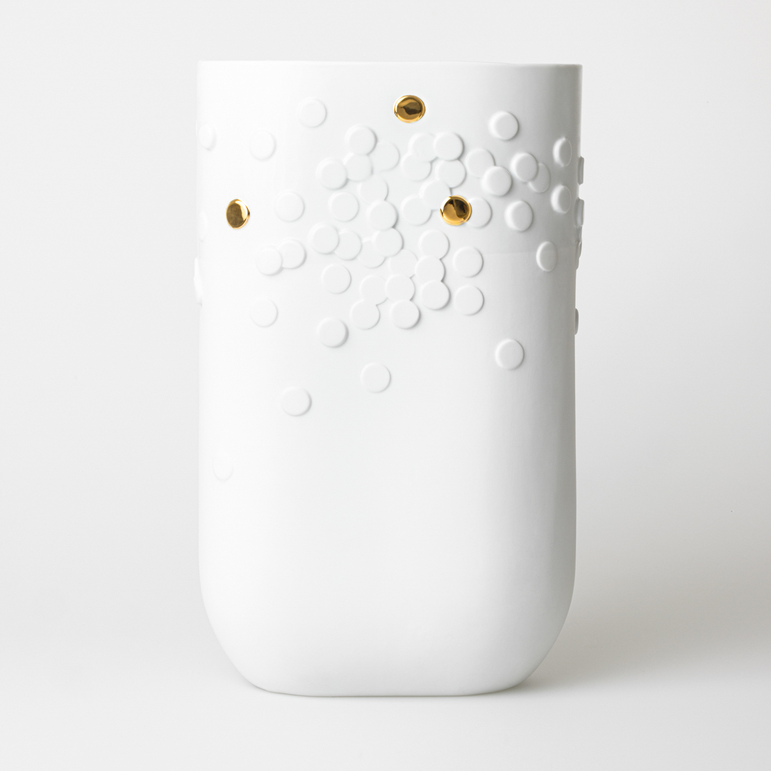 Die Vase ist weiß und zylindrisch mit einer glatten Oberfläche. Sie ist mit erhabenen weißen Punkten und einigen goldenen Akzenten verziert.