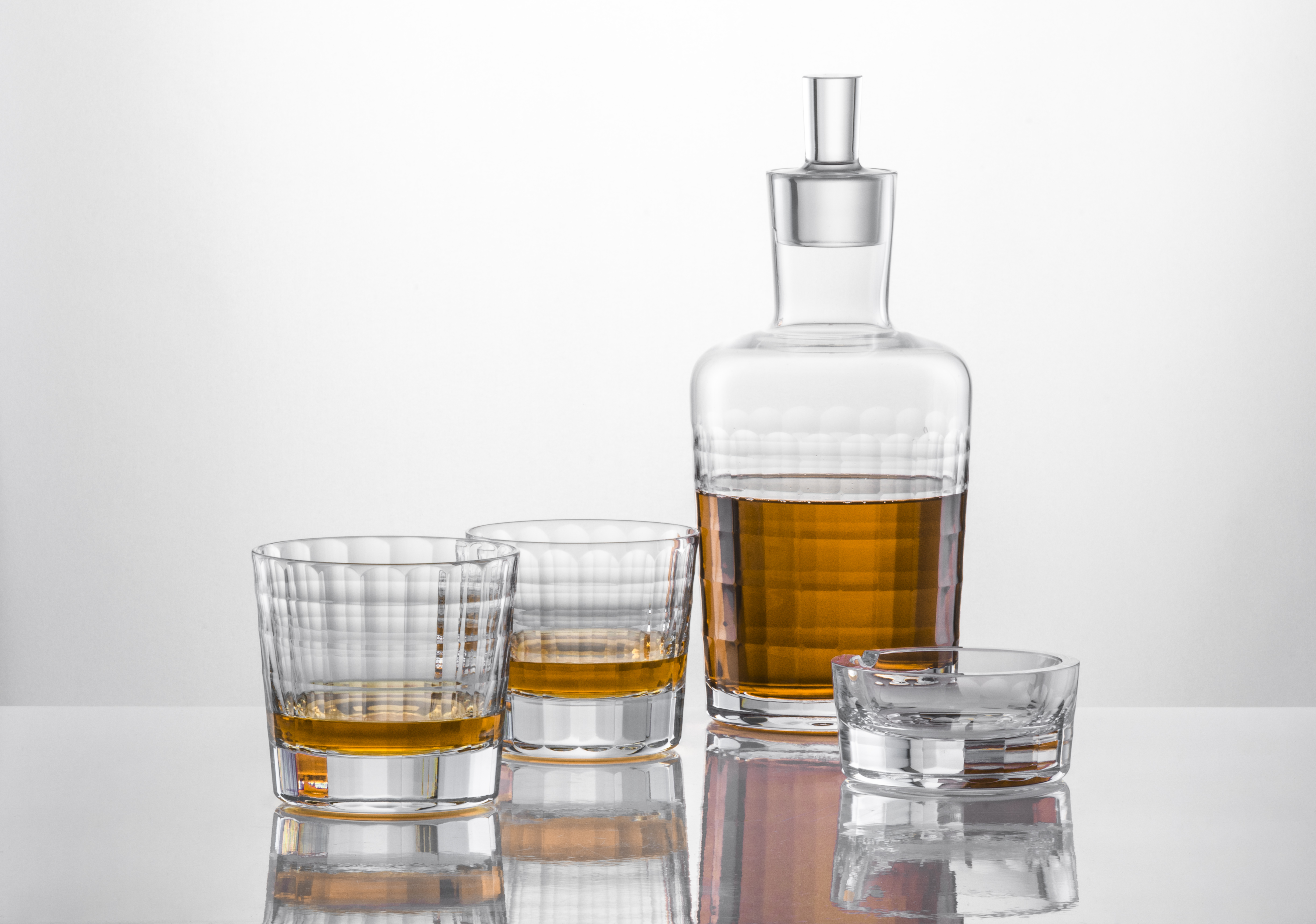 Auf dem Bild sind eine Karaffe und drei Gläser aus klarem Glas zu sehen. In der Karaffe und in zwei der Gläser befindet sich ein braunes Getränk, vermutlich Whisky.