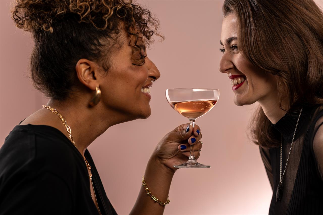 Zwei Frauen lachen sich an, während eine von ihnen ein Sektschale-Glas mit roséfarbenem Getränk hält. Das Glas ist das Produkt „4er Sektschale Bar Special 8“.
