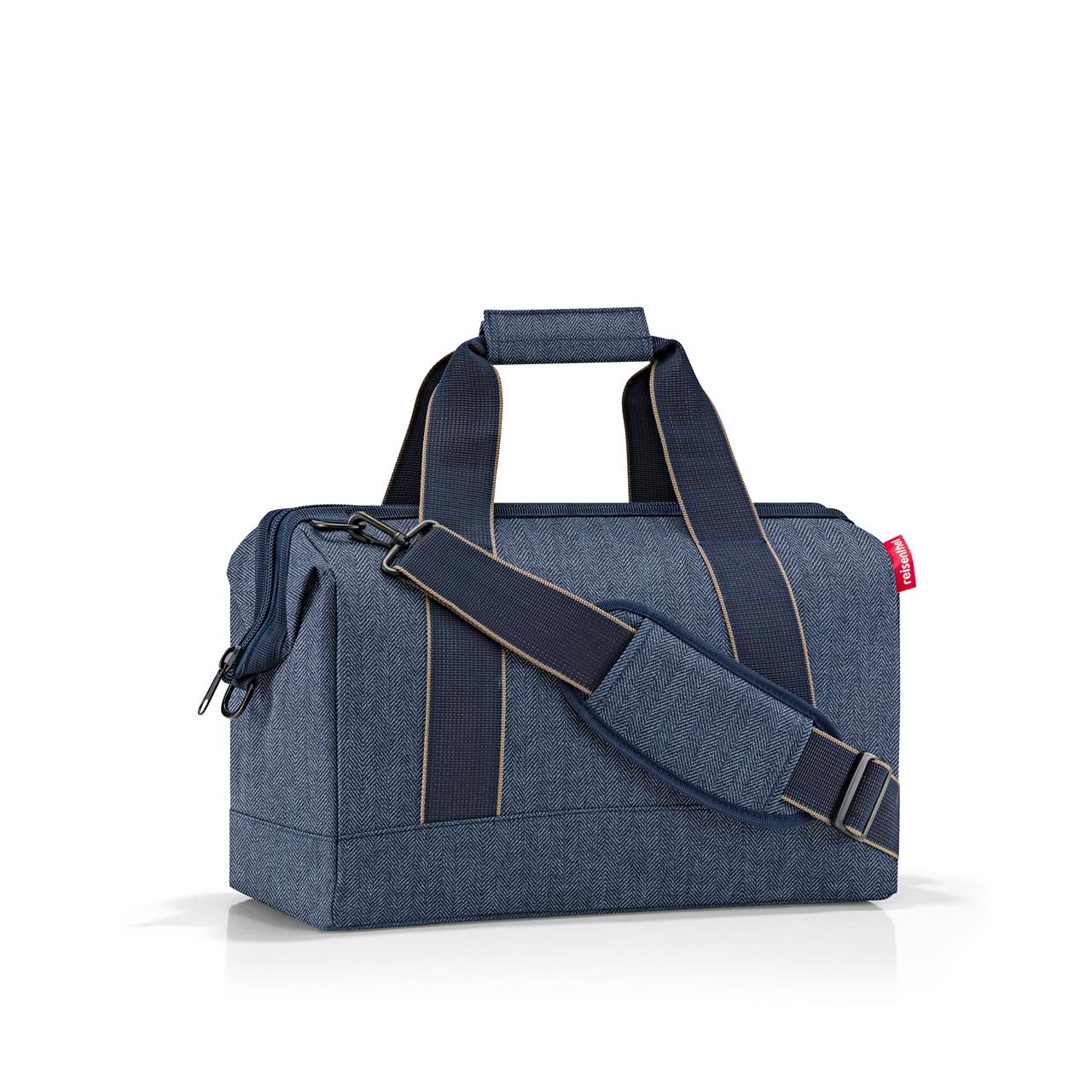 Die Abbildung zeigt eine dunkelblaue Reisetasche mit Herringbone-Muster und zwei Tragegriffen sowie einem Schultergurt. Die Tasche wirkt modern und funktional.